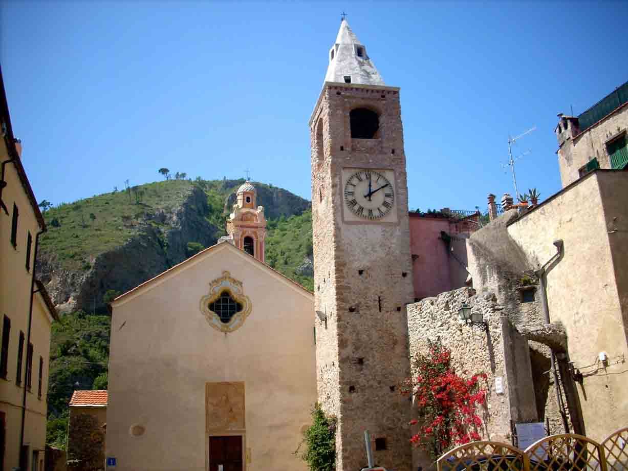 Campanile in pietra con orologio accanto alla chiesa, collina verde sullo sfondo