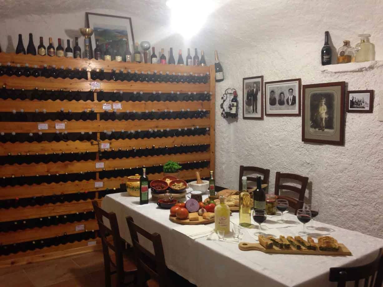 Cantina con bottiglie di vino su scaffali di legno e tavola imbandita