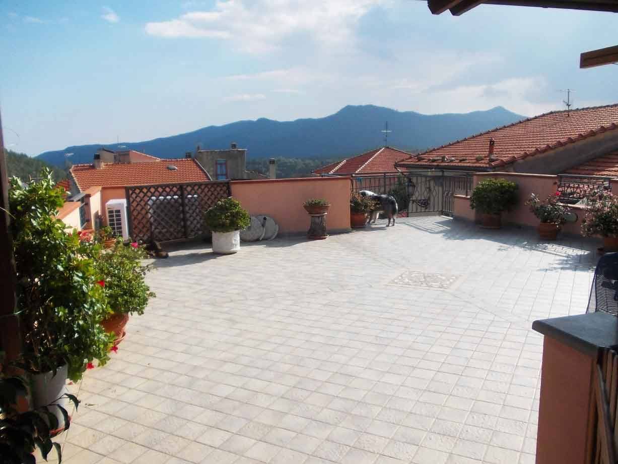 Terrazza piastrellata con vasi di fiori, tetti rossi e monti sullo sfondo