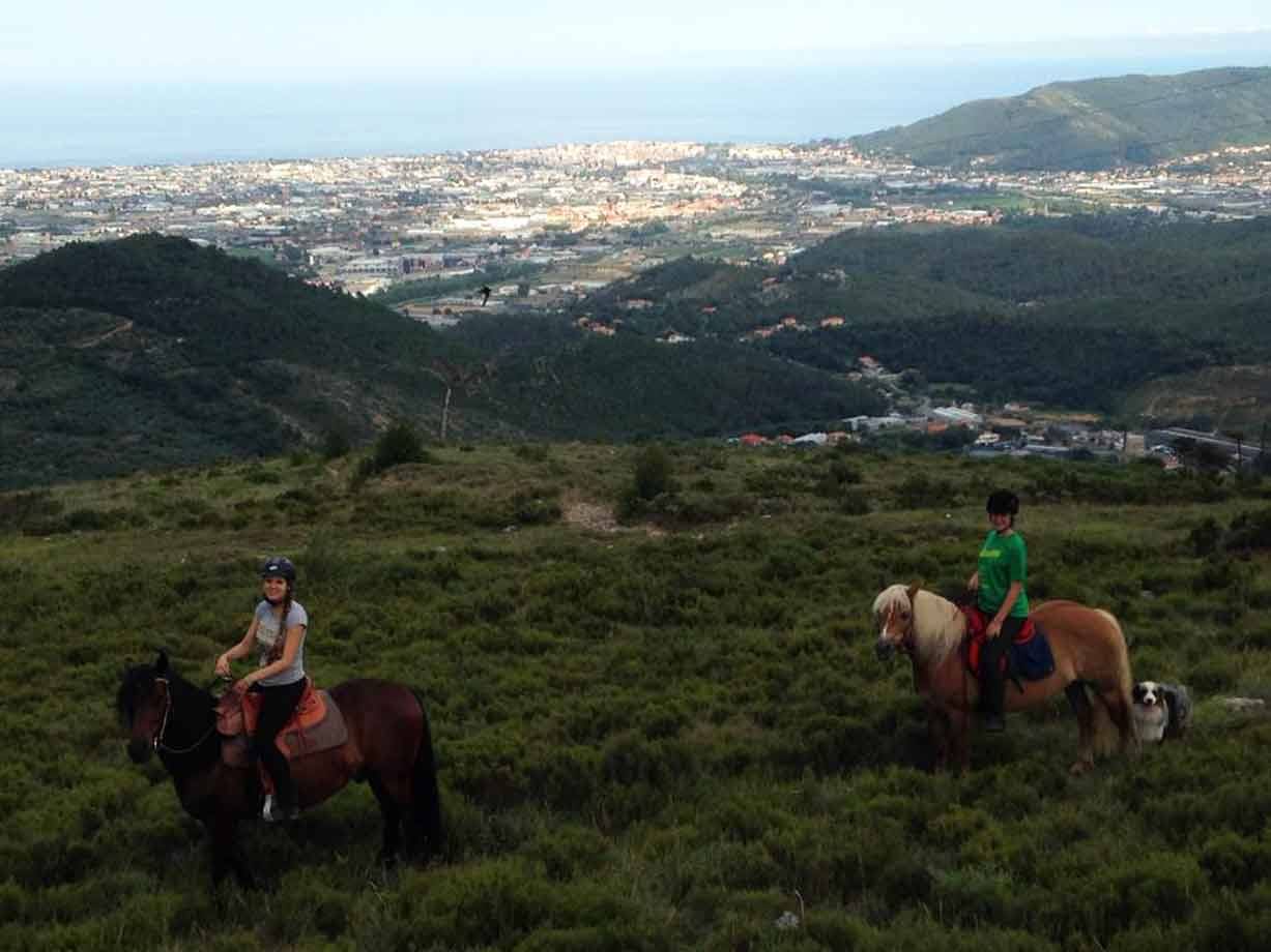 Due cavalieri a cavallo su collina verde sopra la città, con un cane