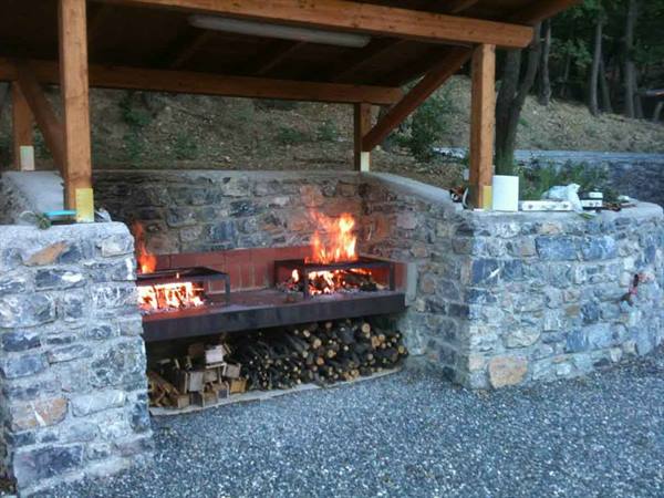 Stone barbecue with burning fire under a wooden shelter