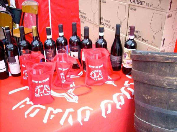 Red wine bottles on red-clothed table, glasses in red bags, wooden barrel