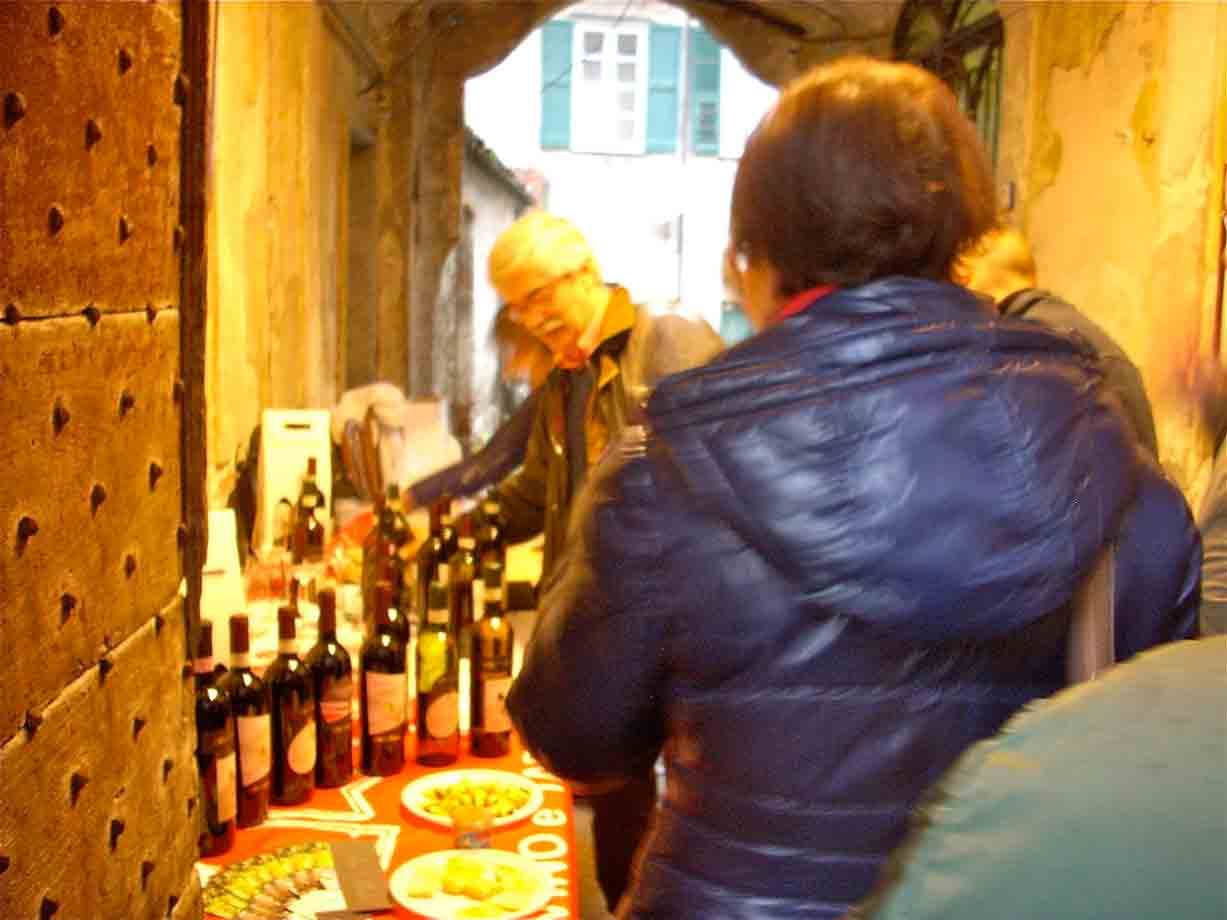 Degustazione di vino tra bottiglie e cibo in un vicolo con portale antico
