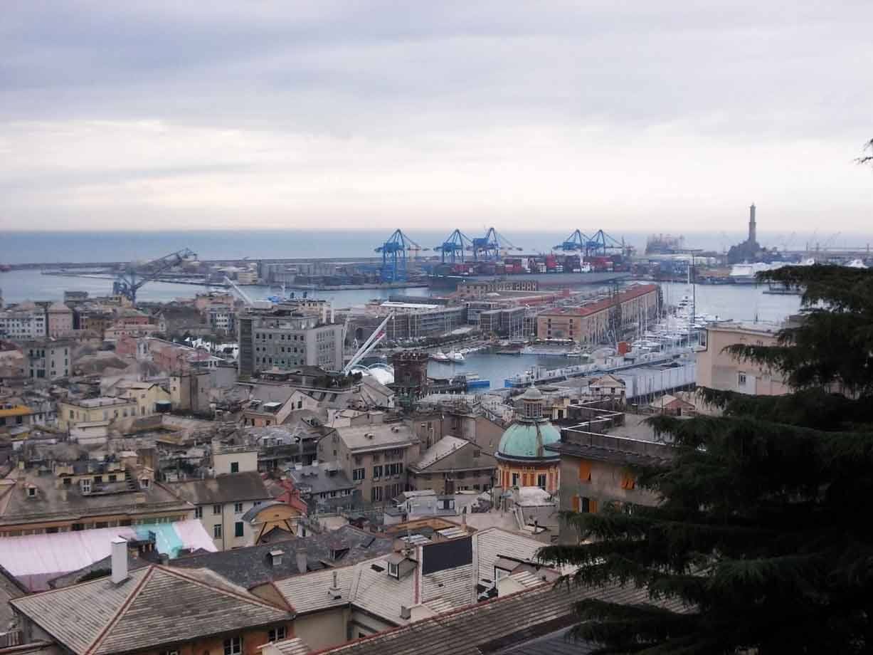 Il porto di Genova con gru blu, il faro Lanterna e i tetti sotto il cielo grigio