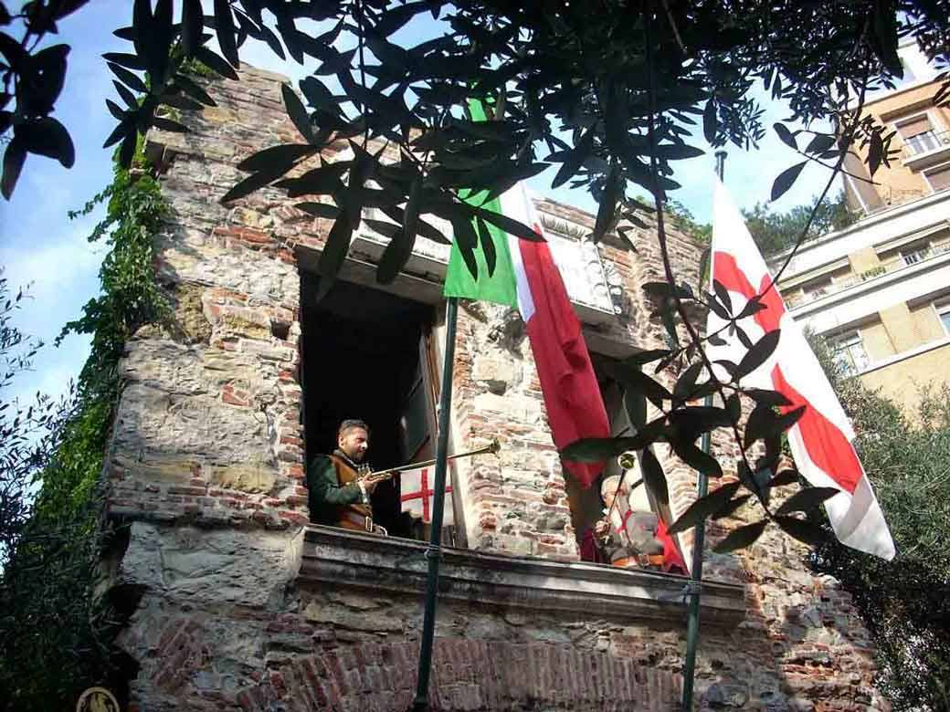 Trombettiere in costume medievale sulla Porta Soprana a Genova, tra bandiere