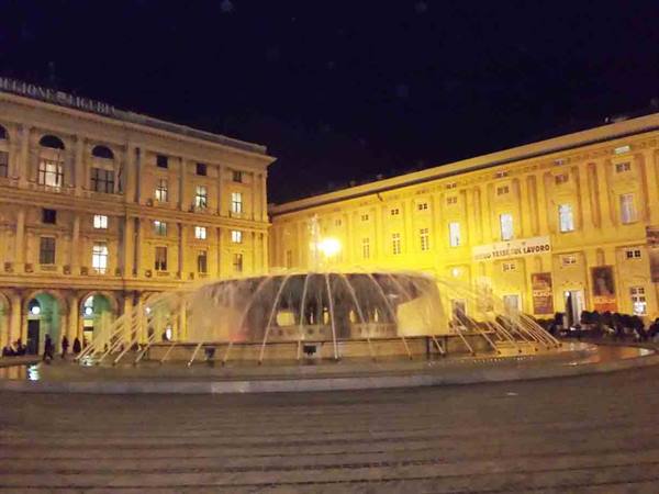 Illuminated fountain at Piazza De Ferrari, Genoa, with historic buildings at night