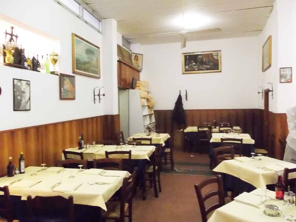 Sala di trattoria con tavoli apparecchiati, tovaglie gialle, sedie in legno e quadri alle pareti