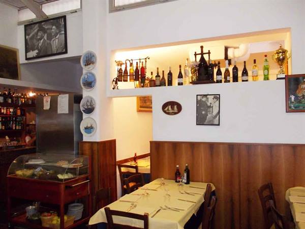 Trattoria dining room with set tables, lit bottles and decorative plates on walls