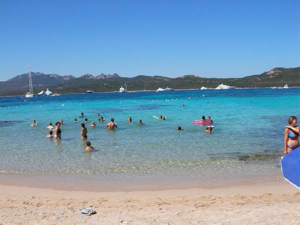 Swimmers in turquoise water with anchored yachts, white sand beach, Costa Smeralda