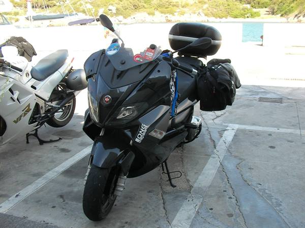 Black Gilera scooter with travel bags, parked next to a white motorcycle