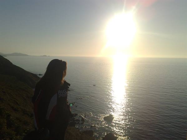 Girl silhouetted on rocky coast facing the low sun over the sea