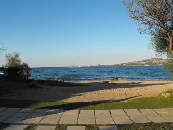 Sandy beach with tiled plaza, trees and blue sea, boats in the distance