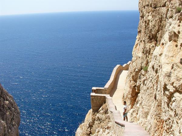 Stone staircase carved into the cliff, man descending toward the blue sea