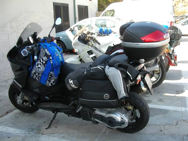Black scooter loaded with luggage and helmets, parked beside touring motorcycles