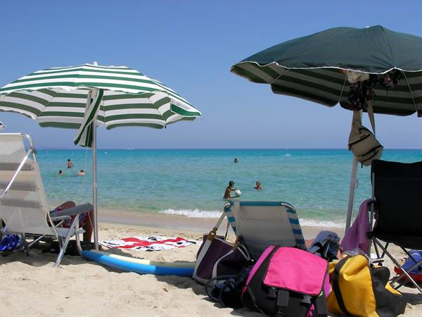 Striped umbrellas on light sand, swimmers in the turquoise sea