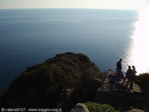 Hikers on granite rocks above the sea, bright sunlight on the water