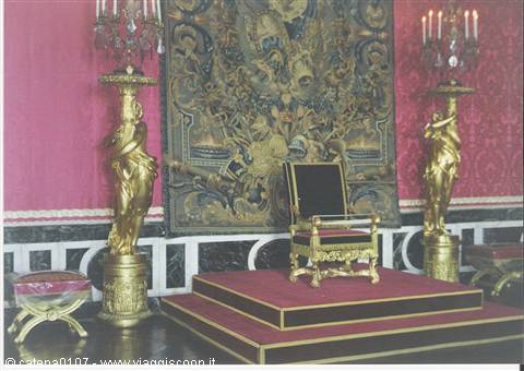 Gilded throne on red platform between golden statues and historic tapestry in royal palace