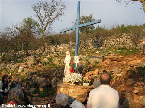 Pilgrims praying before a blue cross and Madonna statue on rocky hillside, Medjugorje