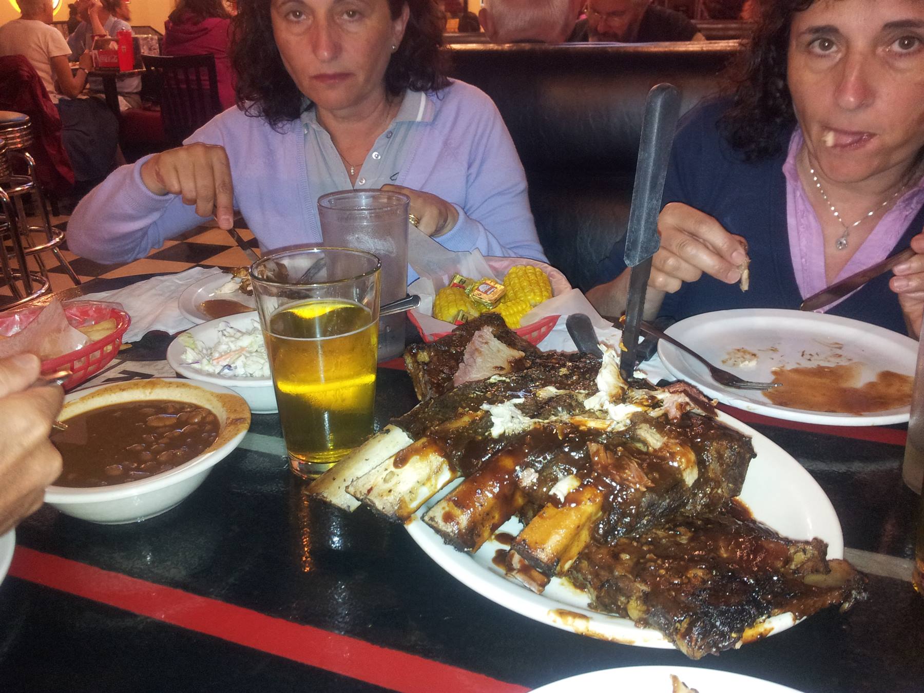 Two women eating BBQ ribs at an American diner, beer and chili on the table