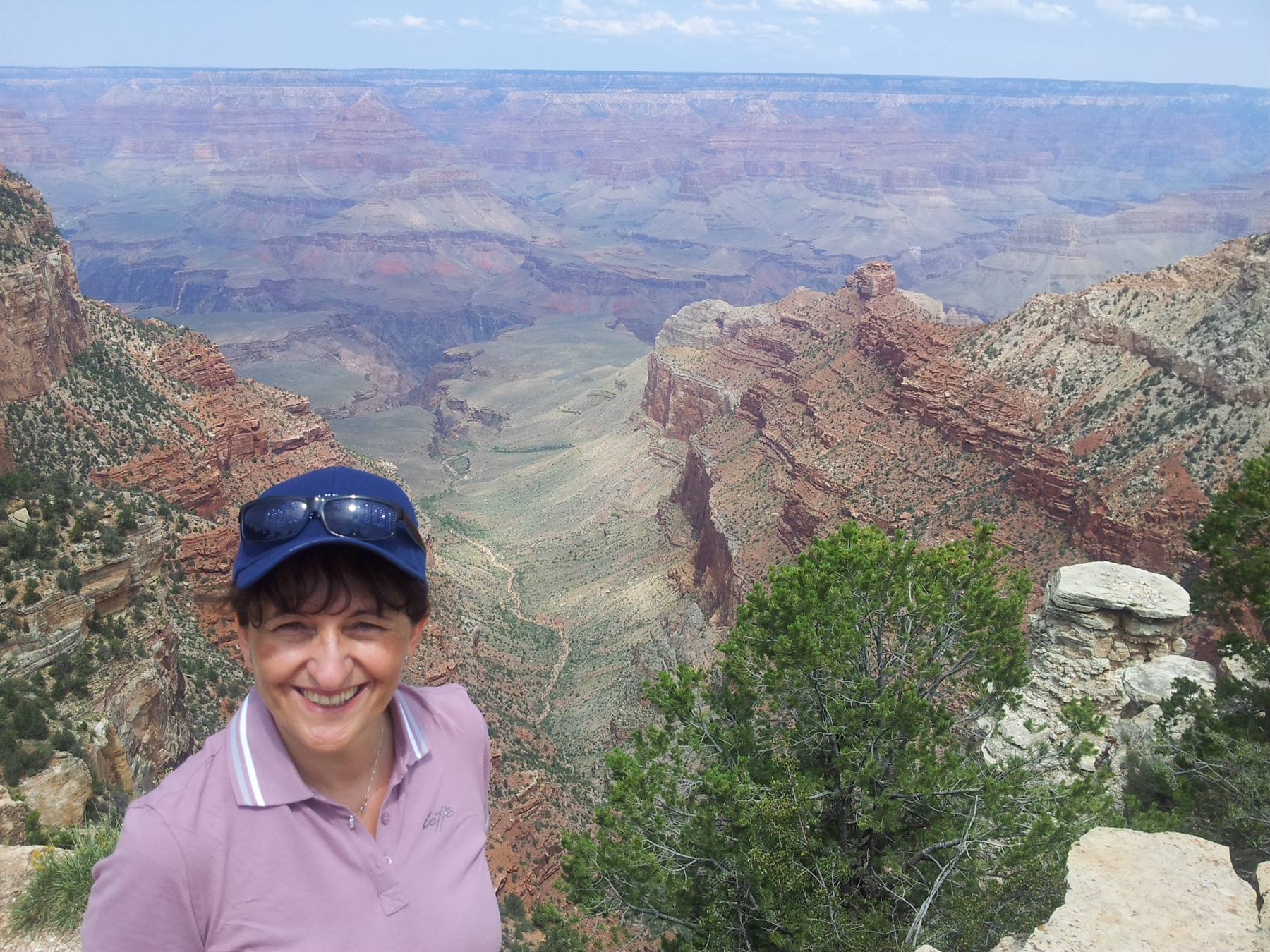 Smiling woman in blue cap and sunglasses before the red rocks of Grand Canyon