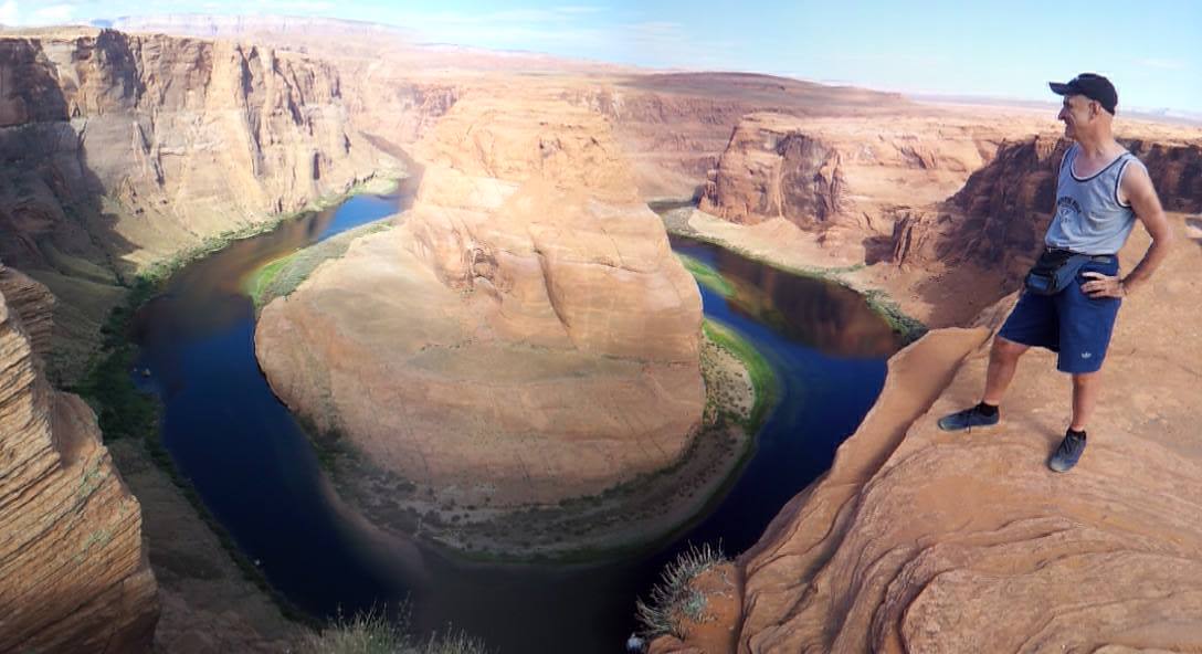 Tourist standing on the sandstone rim of Horseshoe Bend as the Colorado River curves below
