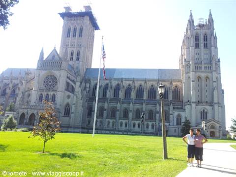 Two tourists walking past the Gothic stone facade of Washington National Cathedral