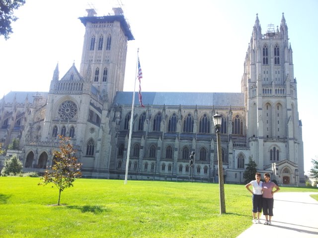 Two tourists walking past the Gothic stone facade of Washington National Cathedral