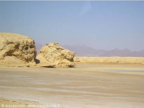 Sandy rock formations on the beach, hazy mountains behind, bright sunlight