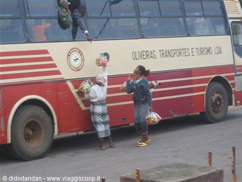 Women vendors carrying baskets on heads beside a red and cream bus