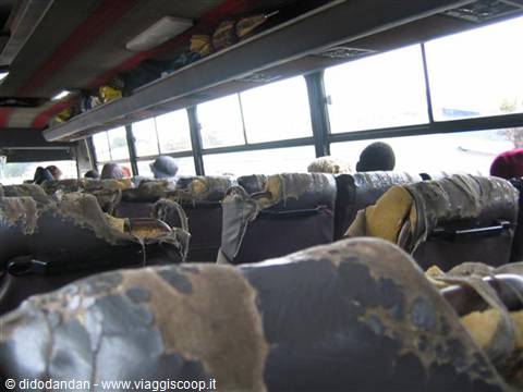 Inside a worn bus with tattered rubber seats and passengers seated