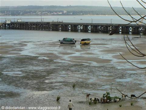 Two boats stranded on sand at low tide in front of wooden pier