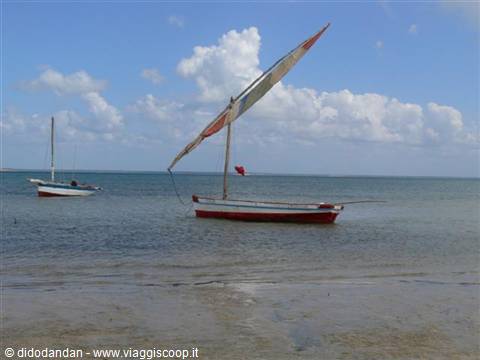 Red and white sailboat anchored near the shore, another boat in the background
