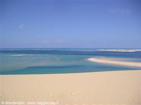 Pale sand dune above turquoise lagoon and ocean under blue sky
