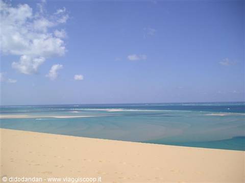 Golden sand dune over turquoise waters, blue sky with clouds
