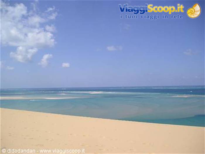 Golden sand dune over turquoise waters, blue sky with clouds