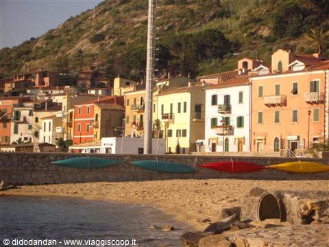 Colorful kayaks resting on the sand in front of Marina di Campo houses
