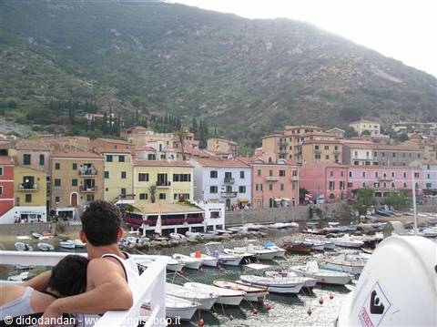 Couple watches boats moored at Giglio harbor among colorful houses