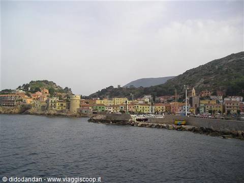 Boats moored at Giglio harbor beneath colorful houses and green hills