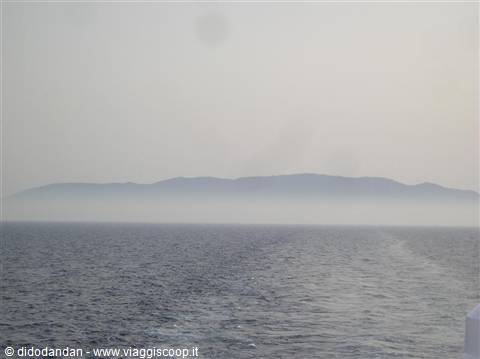 Fog-shrouded island seen from the ferry, wake across the grey sea