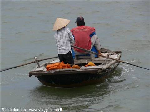 Two fishermen row a wooden boat, one wearing a straw hat