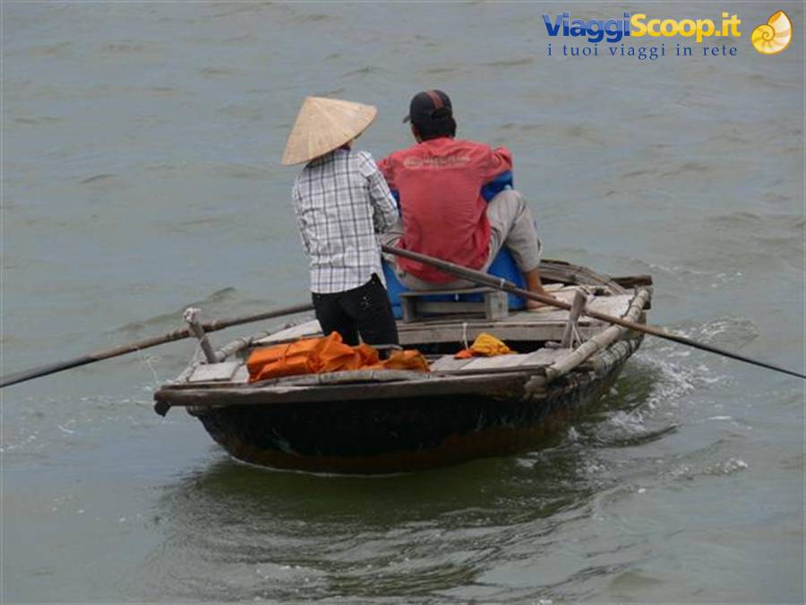 Two fishermen row a wooden boat, one wearing a straw hat