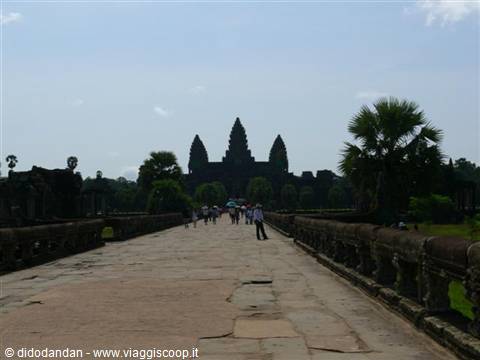 Tourists walk along the stone causeway toward Angkor Wat towers
