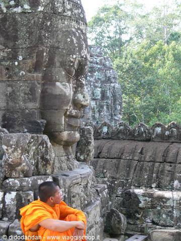 Monk in orange robe sitting beside the giant stone faces of Bayon