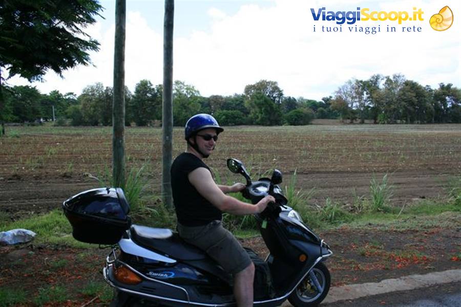Man in blue helmet sitting on a black scooter by a rural road