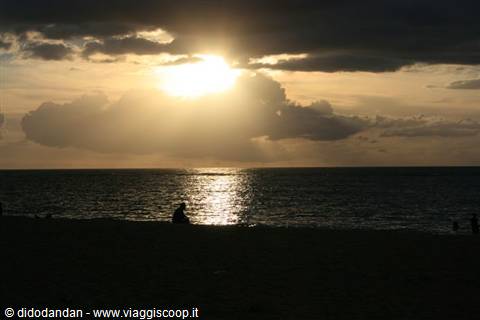 Low sun breaking through clouds over the sea, silhouettes on the beach