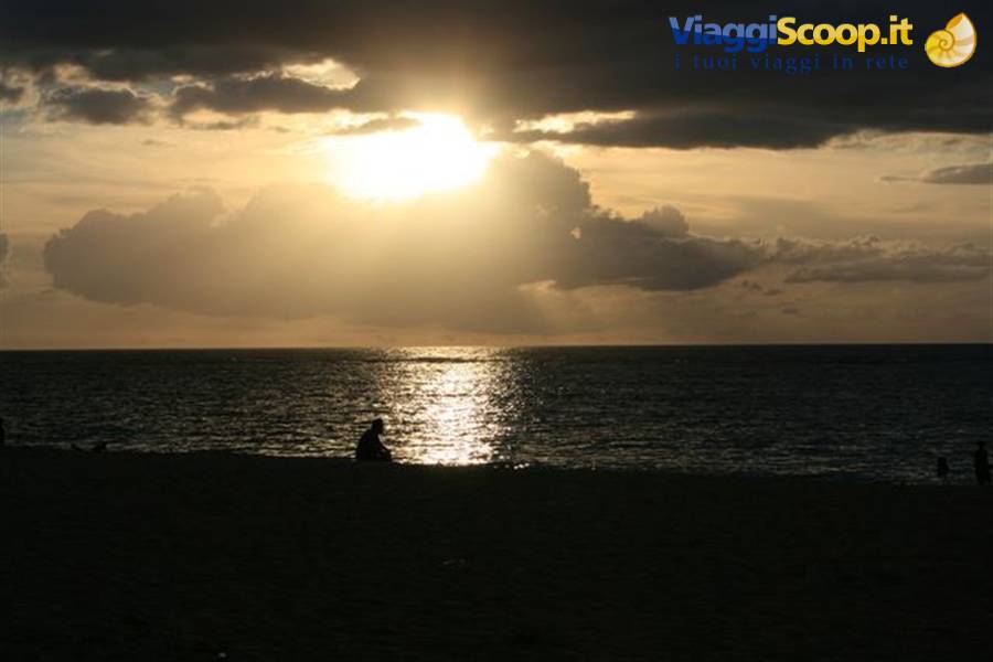 Low sun breaking through clouds over the sea, silhouettes on the beach