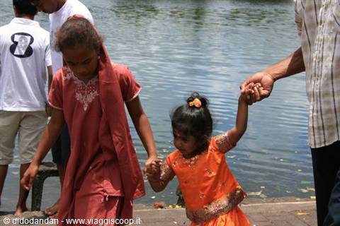 Little girl in orange dress holding hands by the lake water
