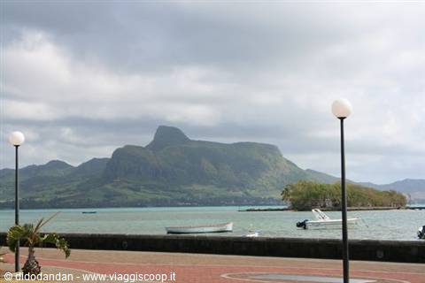 Turquoise lagoon with moored boats and green mountain under clouds in Mauritius