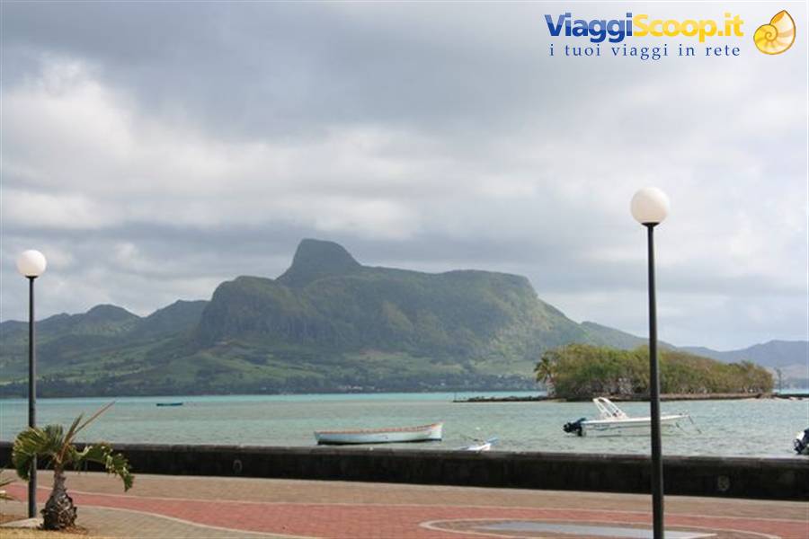 Turquoise lagoon with moored boats and green mountain under clouds in Mauritius