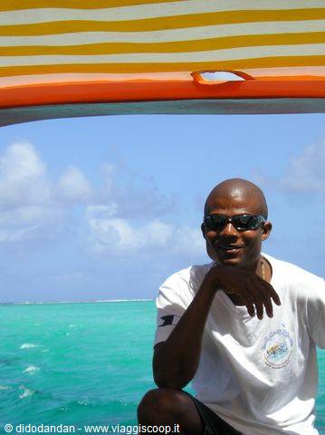 Man in sunglasses on a boat under striped canopy, turquoise sea and blue sky